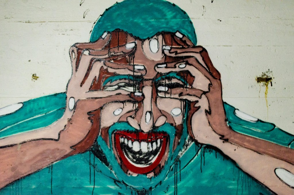 A grafitti painting of a man in blue shirt, holding his hands on his face. Visibly stressed.
